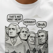 A man wearing black sunglasses and a white graphic t-shirt with a historical parody print of Mount Rushmore, drinking from a paper coffee cup outdoors on a park bench.