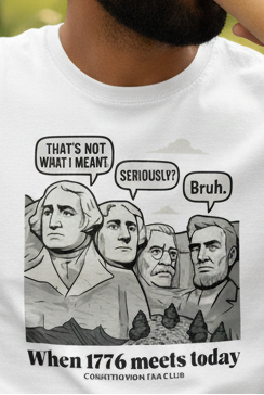 A man wearing black sunglasses and a white graphic t-shirt with a historical parody print of Mount Rushmore, drinking from a paper coffee cup outdoors on a park bench.
